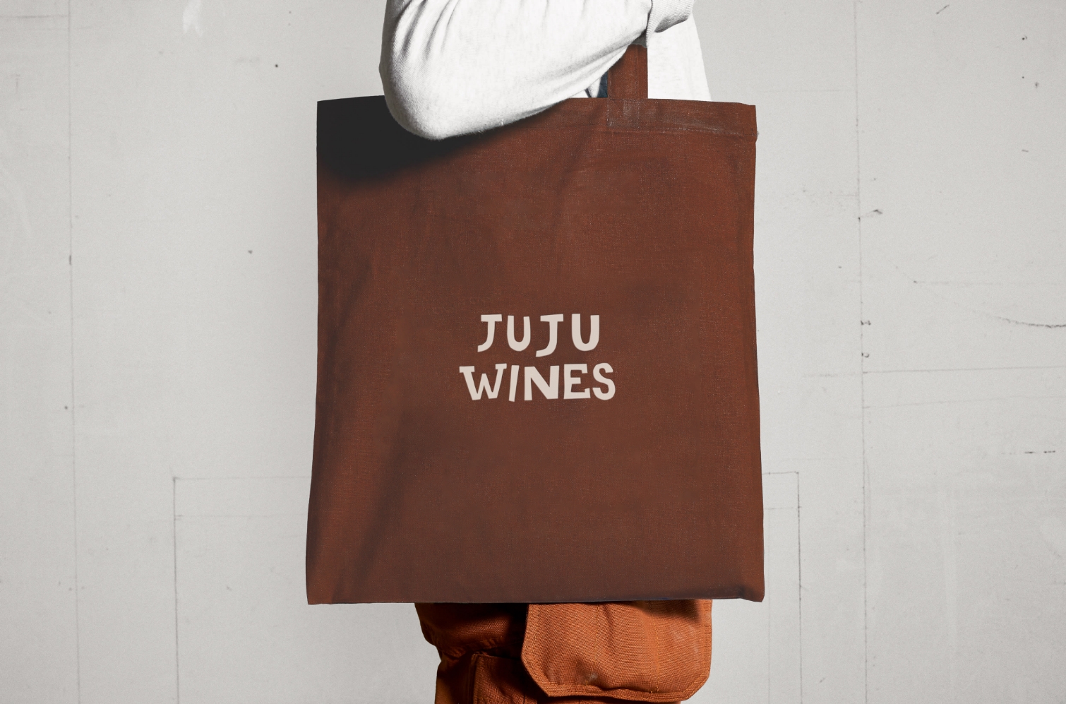 Person holding a brown tote bag with JuJu Vins logo on it