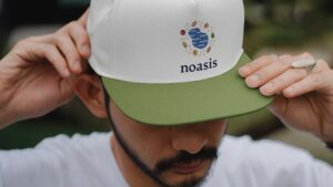 Man wearing green-tipped hat with Noasis Logo